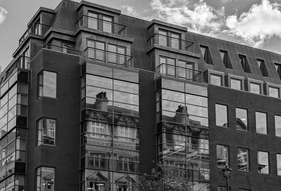 The image depicts the front entrance of a multi-storey residential building with a red brick facade accented by white decorative stone embellishments. There is a large black front door situated within
